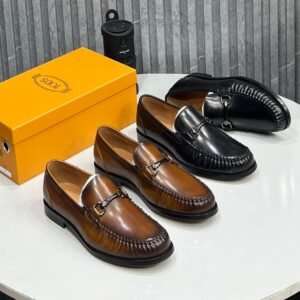 A stylish display of brown and black leather loafers with buckle details, accompanied by a yellow shoe box on a white table.