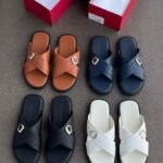 A collection of stylish crisscross strap slides in brown, black, navy blue, and white, displayed with shoe boxes on a grey surface.