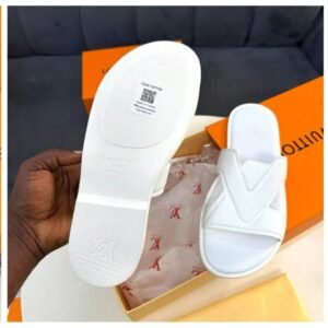 A close-up shot of a pair of white slide sandals with a Louis Vuitton-inspired design, showcasing the sole and the shoe's sleek design, with a hand holding the sandal and a box in the background.
