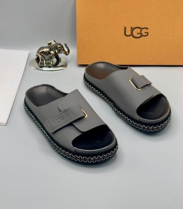 Grey UGG slide sandals with zigzag stitching and gold buckle on a white background, Jsfootis