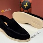 A pair of black suede loafers with cream-colored soles, displayed on a white surface with a brown background, showcasing the Jsfootis brand's commitment to luxury footwear.