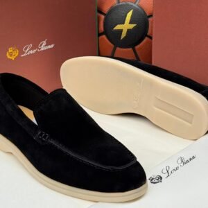 A pair of black suede loafers with cream-colored soles, displayed on a white surface with a brown background, showcasing the Jsfootis brand's commitment to luxury footwear.
