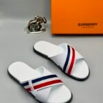 A pair of white slide sandals with red and blue stripes, alongside a Burberry box and a silver elephant figurine, showcasing luxury and style.