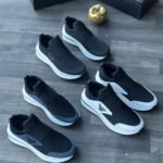 A collection of black and white sneakers arranged on a wooden floor, showcasing the sleek design and comfort of Jsfootis footwear.