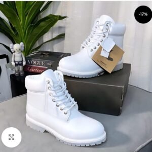 High-quality white leather boots with laces and a chunky sole, displayed on a table with a shoe box and stylish accessories.