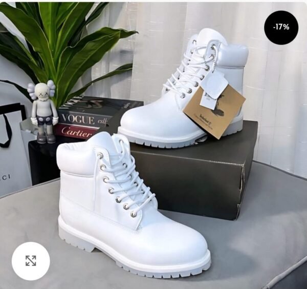 High-quality white leather boots with laces and a chunky sole, displayed on a table with a shoe box and stylish accessories.