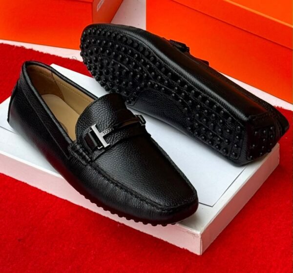 A pair of stylish grey leather loafers with black studs on the sole, displayed on a white shoe box with an orange background, showcasing Jsfootis luxury footwear.
