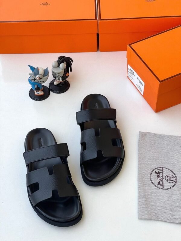 Luxurious black slides with two wide straps, presented with orange shoe boxes and accessories, embodying JC Luxury Footwears' high-end style.