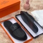 Luxurious black leather slides with H buckle, presented in an orange Hermes box on a plush beige background, Jsfootis brings you high-end style