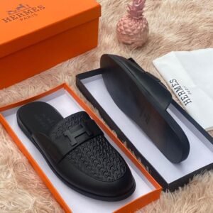 Luxurious black leather slides with H buckle, presented in an orange Hermes box on a plush beige background, Jsfootis brings you high-end style