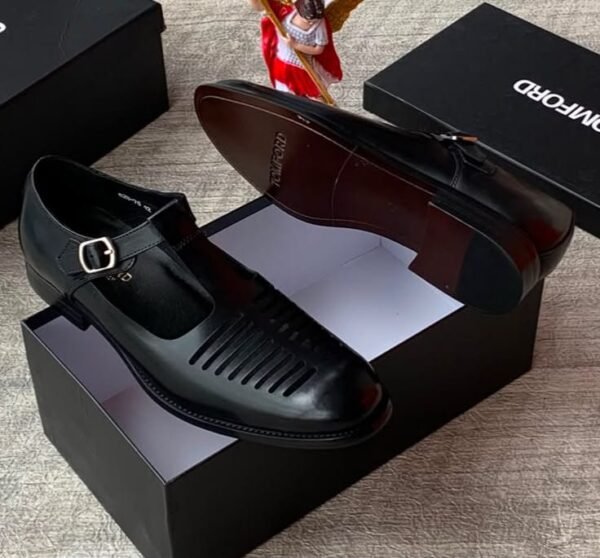 High-quality black leather monk strap shoes with a sleek buckle and ventilation holes, presented on a black shoe box with a reflective surface.