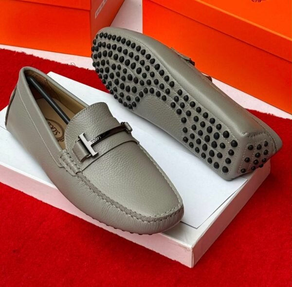root A pair of stylish grey leather loafers with black studs on the sole, displayed on a white shoe box with an orange background, showcasing Jsfootis luxury footwear.
