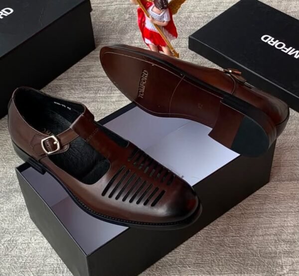 High-quality black leather monk strap shoes with a sleek buckle and ventilation holes, presented on a black shoe box with a reflective surface.