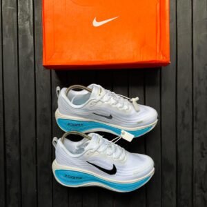 Brand new Nike ZoomX running shoes in white with blue accents and black Nike swoosh logo, displayed with orange Nike shoe box on a dark wooden background | jsfootis