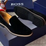 Luxurious black suede loafers with tan soles, presented on a navy blue shoe box with the 'BOSS' logo, embodying JC Luxury Footwears' high-end style.