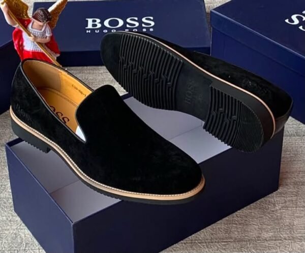 root Luxurious black suede loafers with tan soles, presented on a navy blue shoe box with the 'BOSS' logo, embodying JC Luxury Footwears' high-end style.