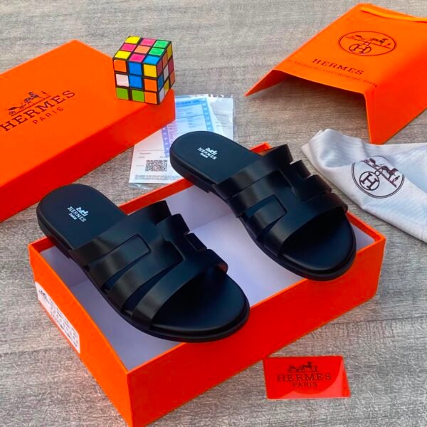 root A pair of black Hermes slides nestled in an orange box, surrounded by luxury accessories.