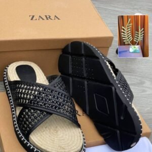 A pair of white slides with woven straps and black outsole, placed on a brown shoe box and cloth with the ZARA logo.