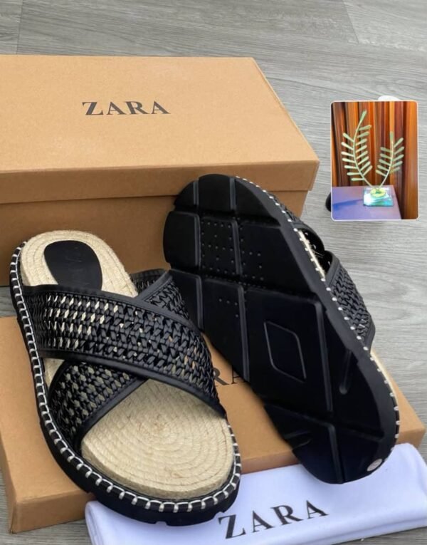 A pair of white slides with woven straps and black outsole, placed on a brown shoe box and cloth with the ZARA logo.