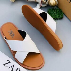 A pair of white ZARA slides with brown soles, displayed on a gray surface with a small astronaut figurine and a ZARA box in the background.